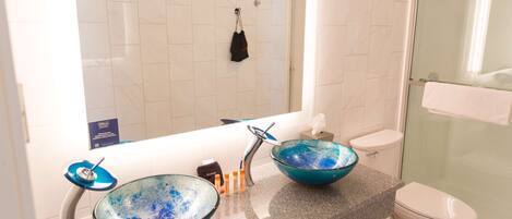 Un baño con dos cuencos de vidrio azul sobre el lavabo, un inodoro blanco y una cabina de ducha con paredes de vidrio.
