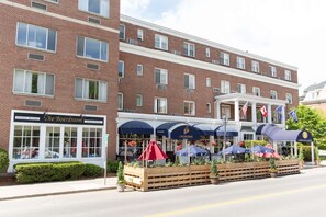 Guests can enjoy a warm welcome at this hotel's inviting entrance, surrounded by lush greenery and shaded by outdoor umbrellas.