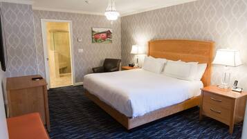 A hotel room with a large bed, two bedside tables with lamps, a wooden nightstand, a chair, and a carpeted floor.