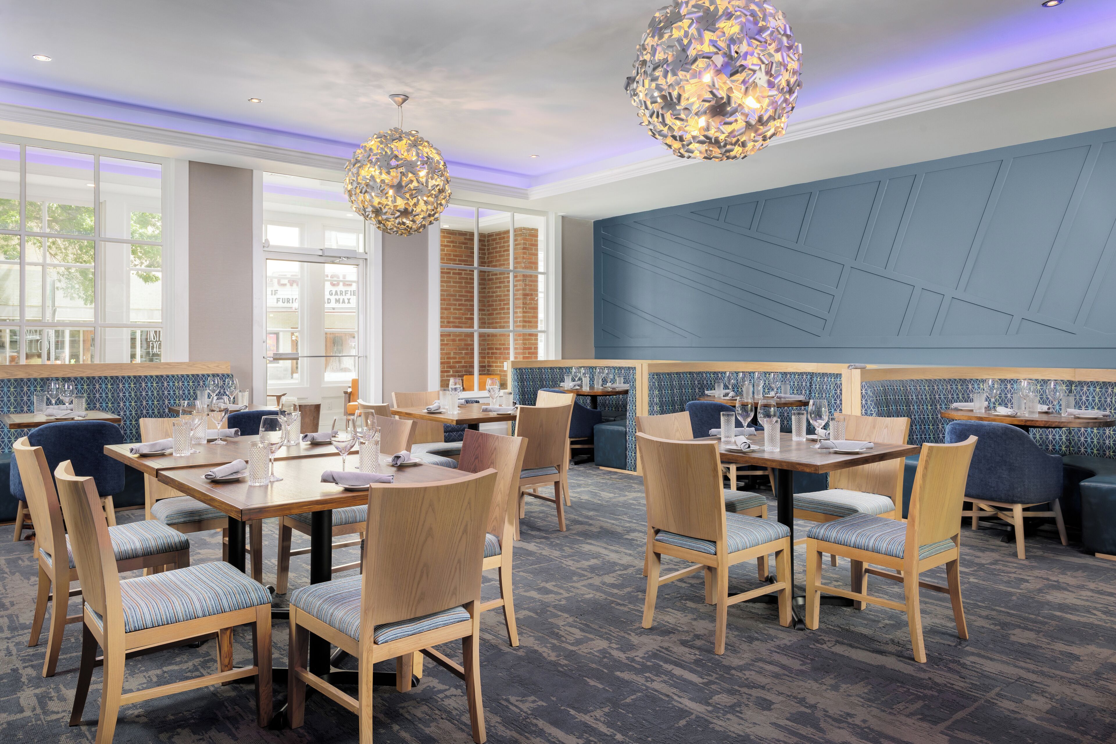 A restaurant with wooden tables and chairs, blue upholstered seating, and decorative hanging lights.
