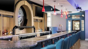 A bar area with a long counter, multiple seating options, and a television mounted on the wall.