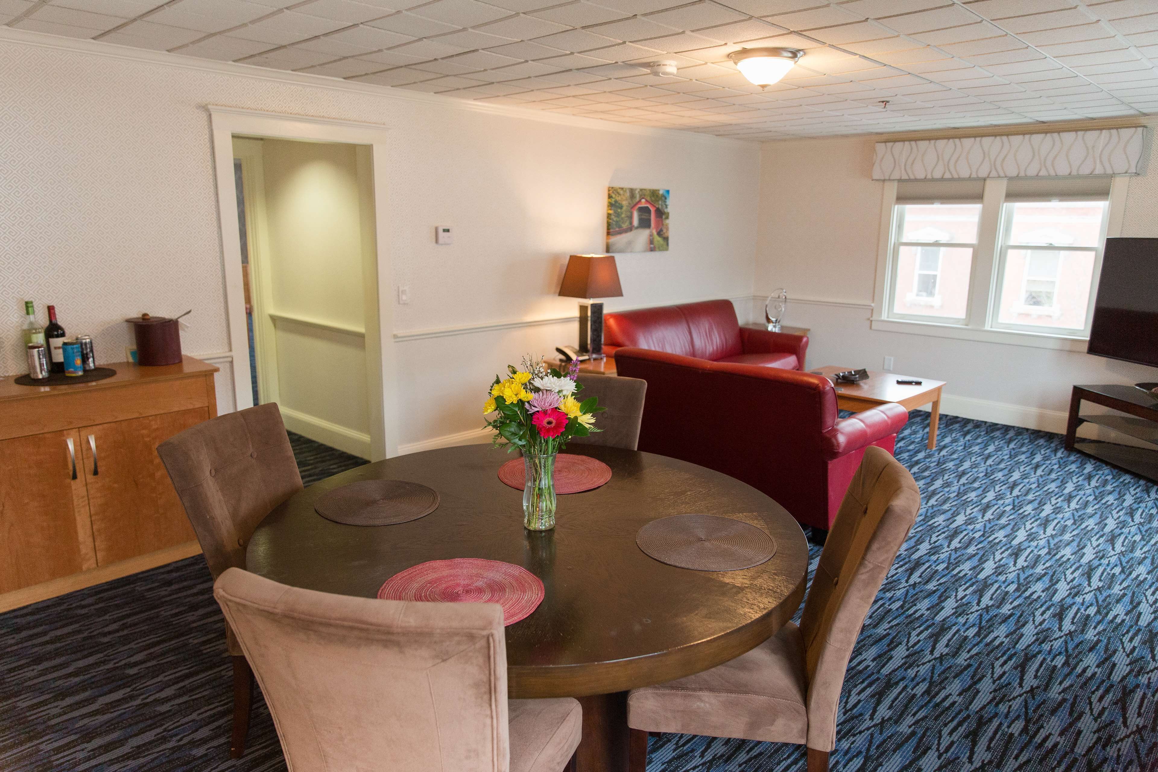 A hotel room with a dining table, chairs, a red sofa, a TV, and a window with a view.