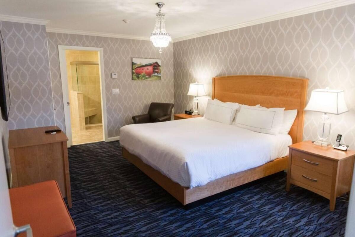 A hotel room with a large bed, two bedside tables, a chair, a desk, and a chandelier.
