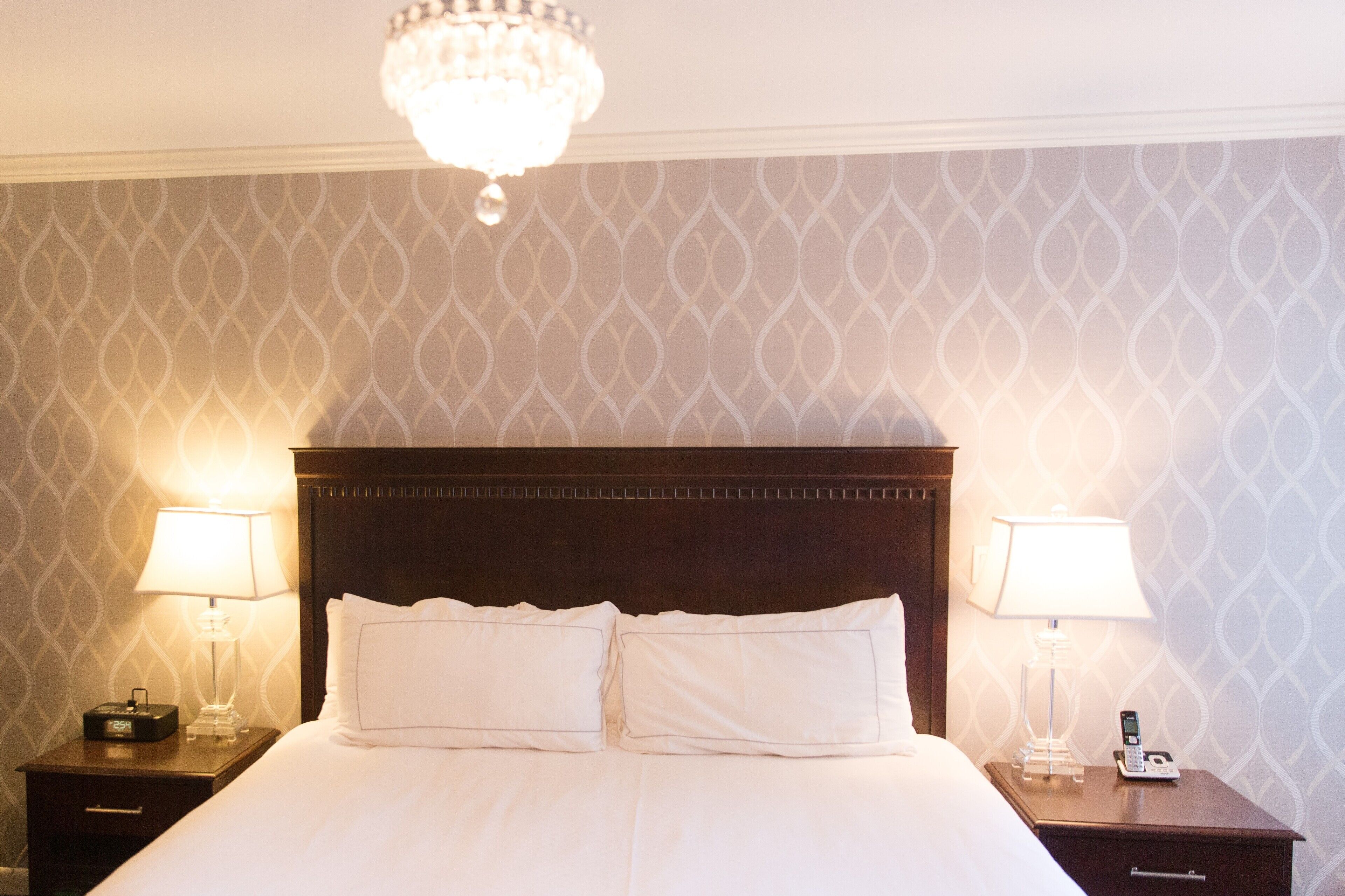 Une chambre d’hôtel avec un grand lit, deux tables de chevet avec des lampes, un lustre et un papier peint à motifs.