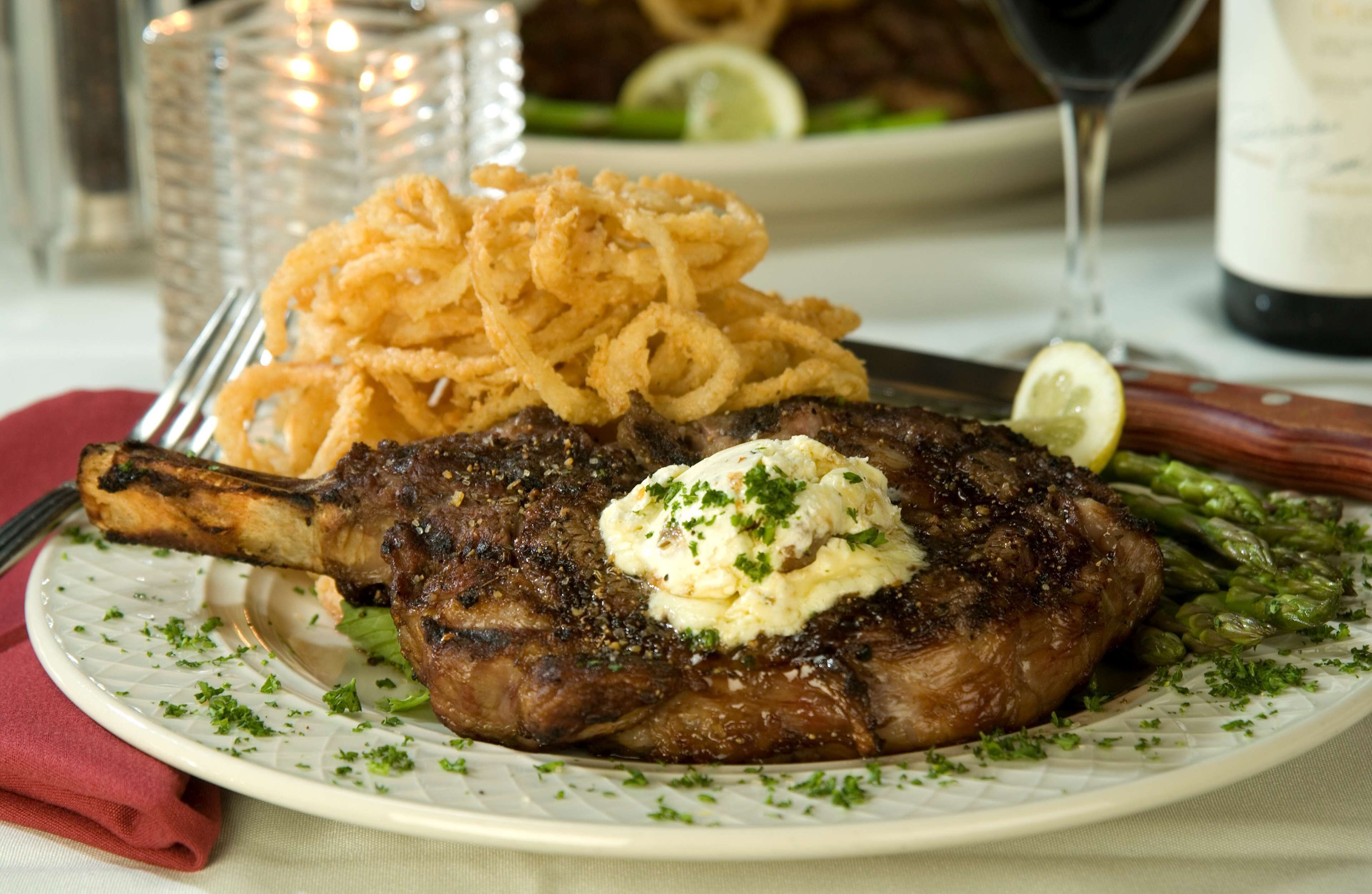 A plate with a steak topped with butter and herbs, accompanied by onion rings and asparagus.