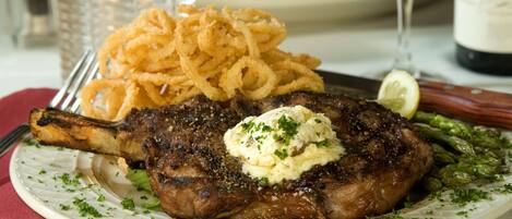 A plate with a steak topped with butter and herbs, accompanied by onion rings and asparagus.