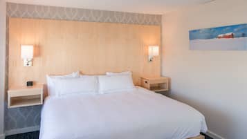 A hotel room with a large bed, two bedside tables, a wall-mounted lamp, and a painting of a snowy landscape.