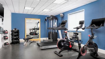 Une salle de sport équipée de machines de cardio, de poids et d’un miroir.