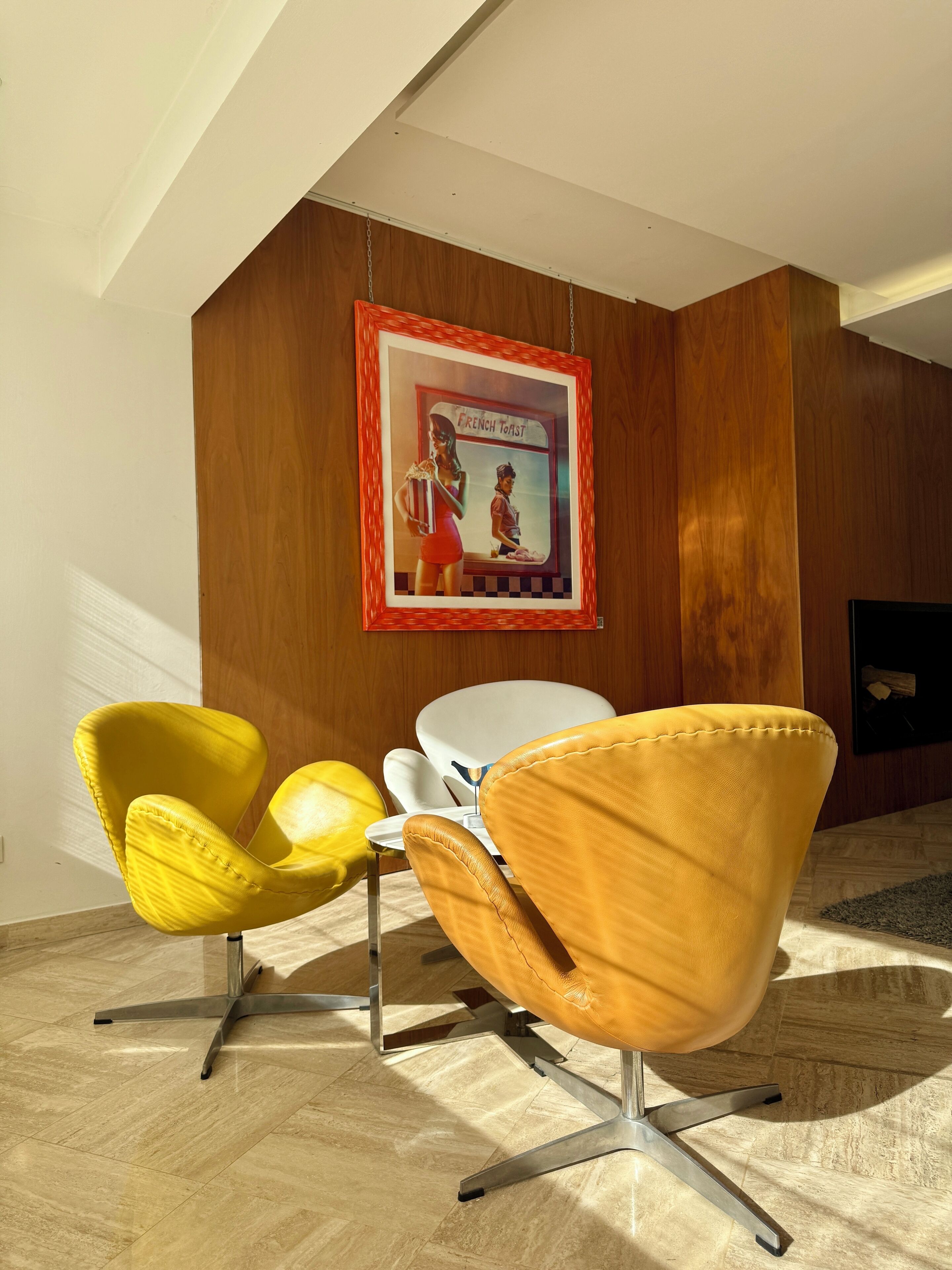 Une pièce moderne avec deux chaises jaunes, une table blanche et un tableau encadré accroché au mur.