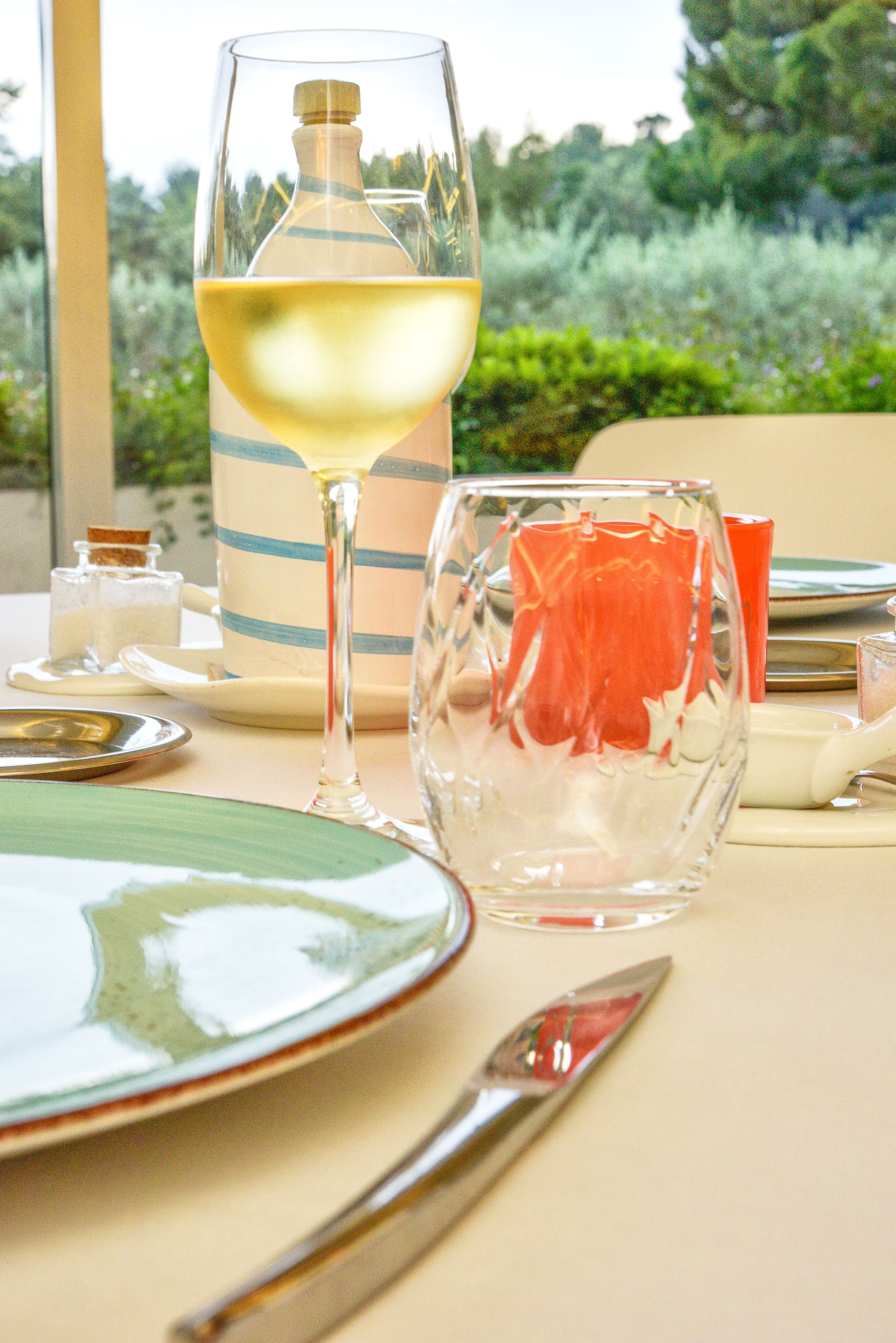 A dining table with a glass of white wine, a striped mug, and a glass with a decorative pattern.