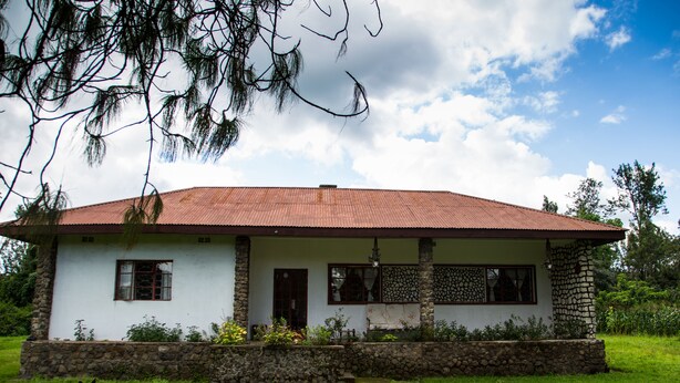 A two-story house with a stone foundation, a red roof, and a front porch.
