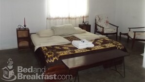 A bedroom with a bed, a chair, a nightstand, and a window with curtains.