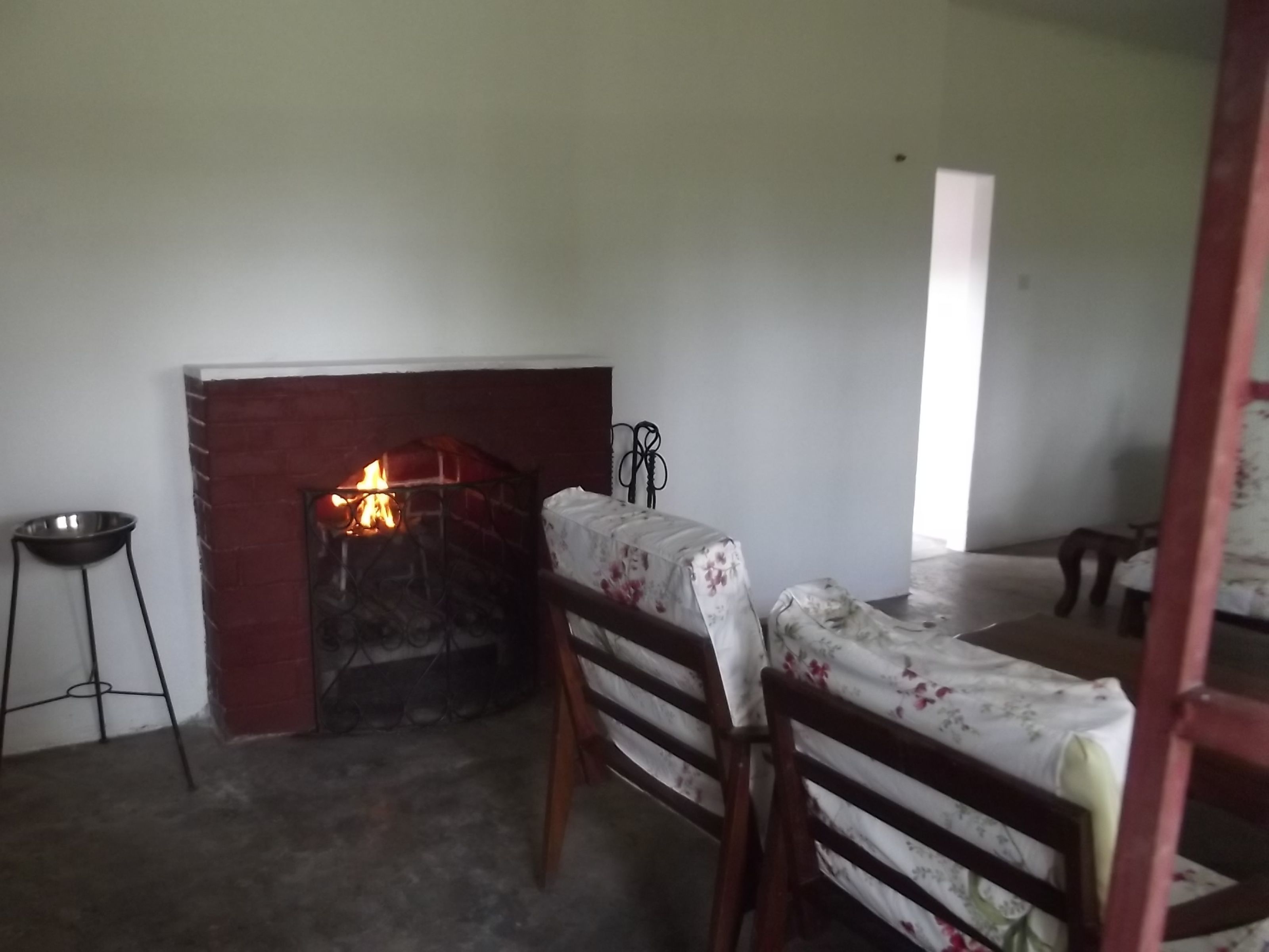 A room with a fireplace, a dining table with chairs, and a metal bowl on a stool.