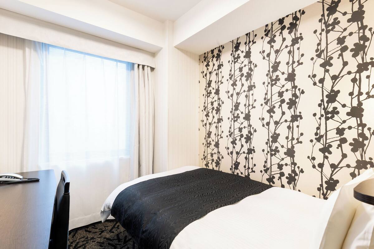 A hotel room with a bed, a desk, and a large window with curtains.