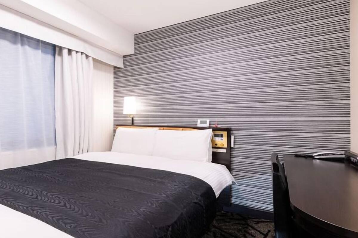 A hotel room with a bed, a desk, a lamp, and a wall with a striped pattern.