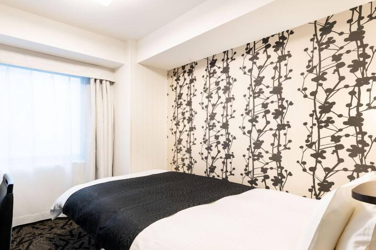 A hotel room with a bed, a desk, and a window with curtains.