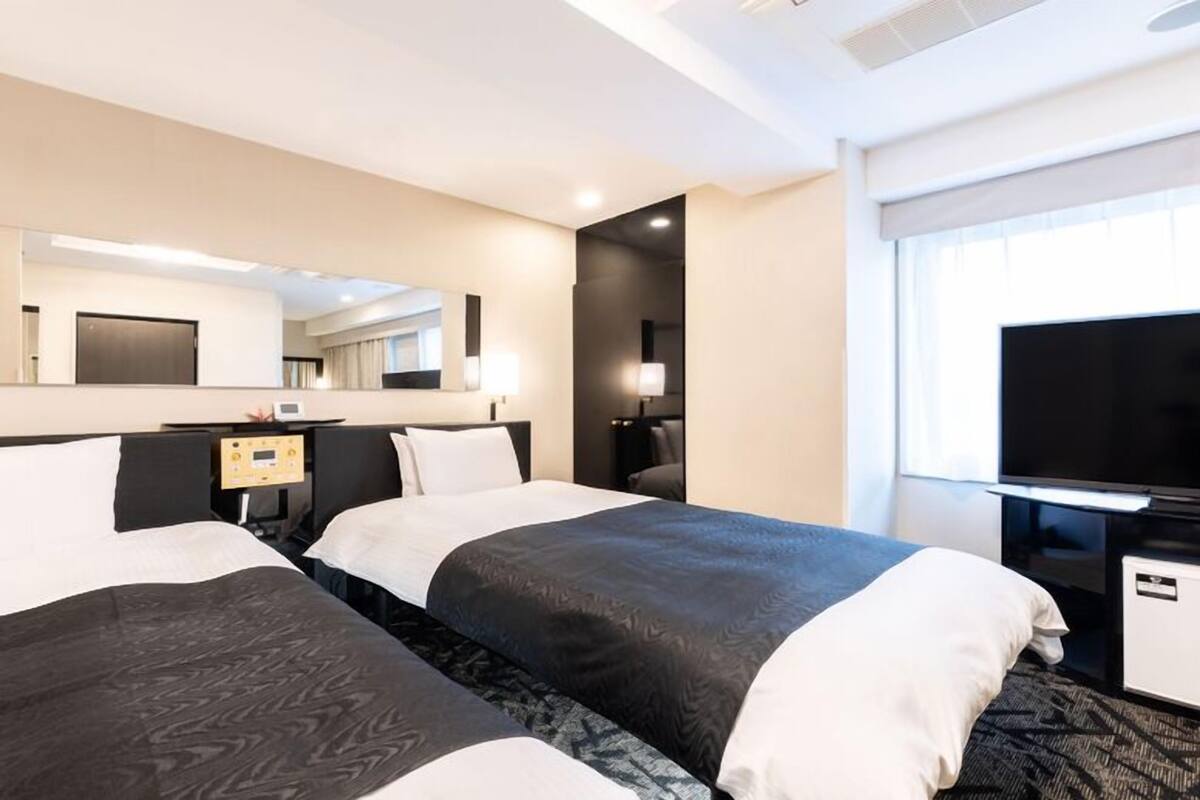 A hotel room with two beds, a TV, a desk, and a mirror.