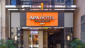 The entrance to APA Hotel with a prominent orange sign, a glass door entrance, and a modern architectural design. - APA Hotel Ginza Shintomicho Ekimae (Tokyo)
