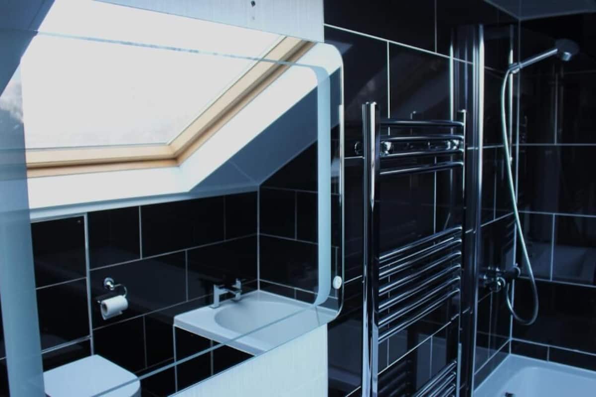 Un baño moderno con tragaluz, cabina de ducha de vidrio y lavamanos blanco.