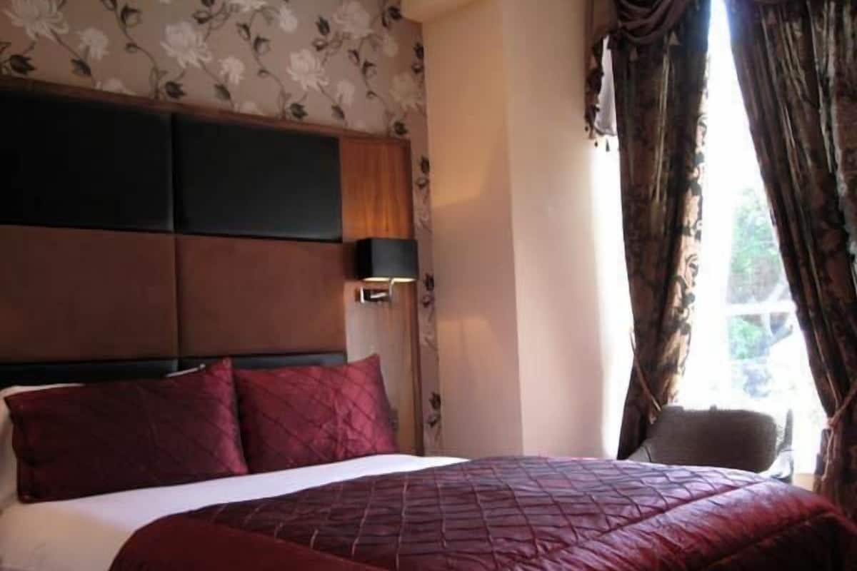 Un dormitorio con una cama grande, cabecera, mesita de noche y ventana con cortinas.