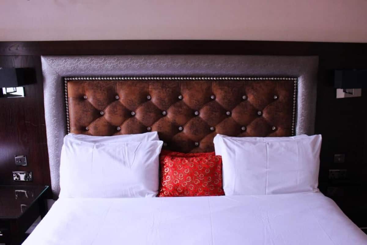 Una cama con cabecera capitonada, almohadas blancas y rojas, y una mesita de noche de madera oscura.