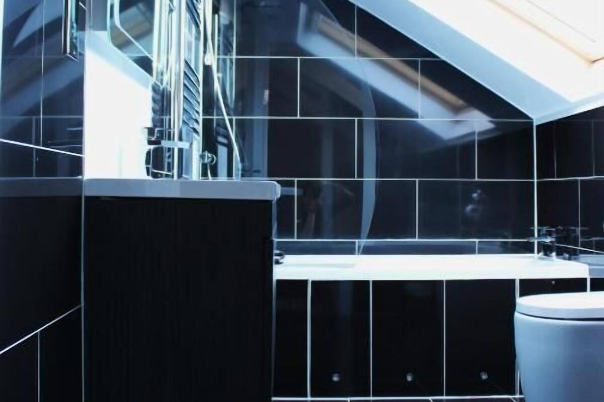 Un baño moderno con baldosas negras, un lavamanos blanco y un tragaluz.