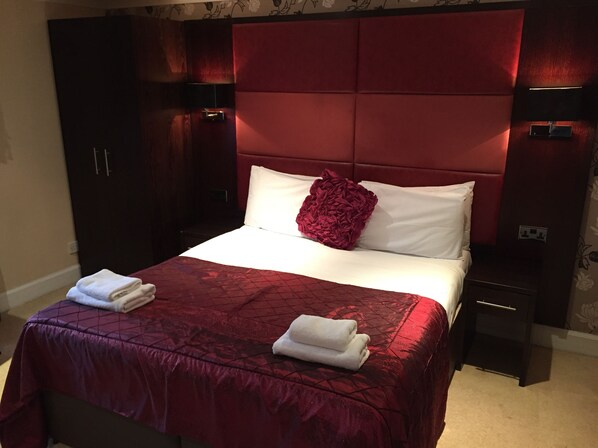 Une chambre d’hôtel avec un grand lit, une literie rouge et blanche, deux tables de chevet avec des lampes et des armoires en bois foncé.