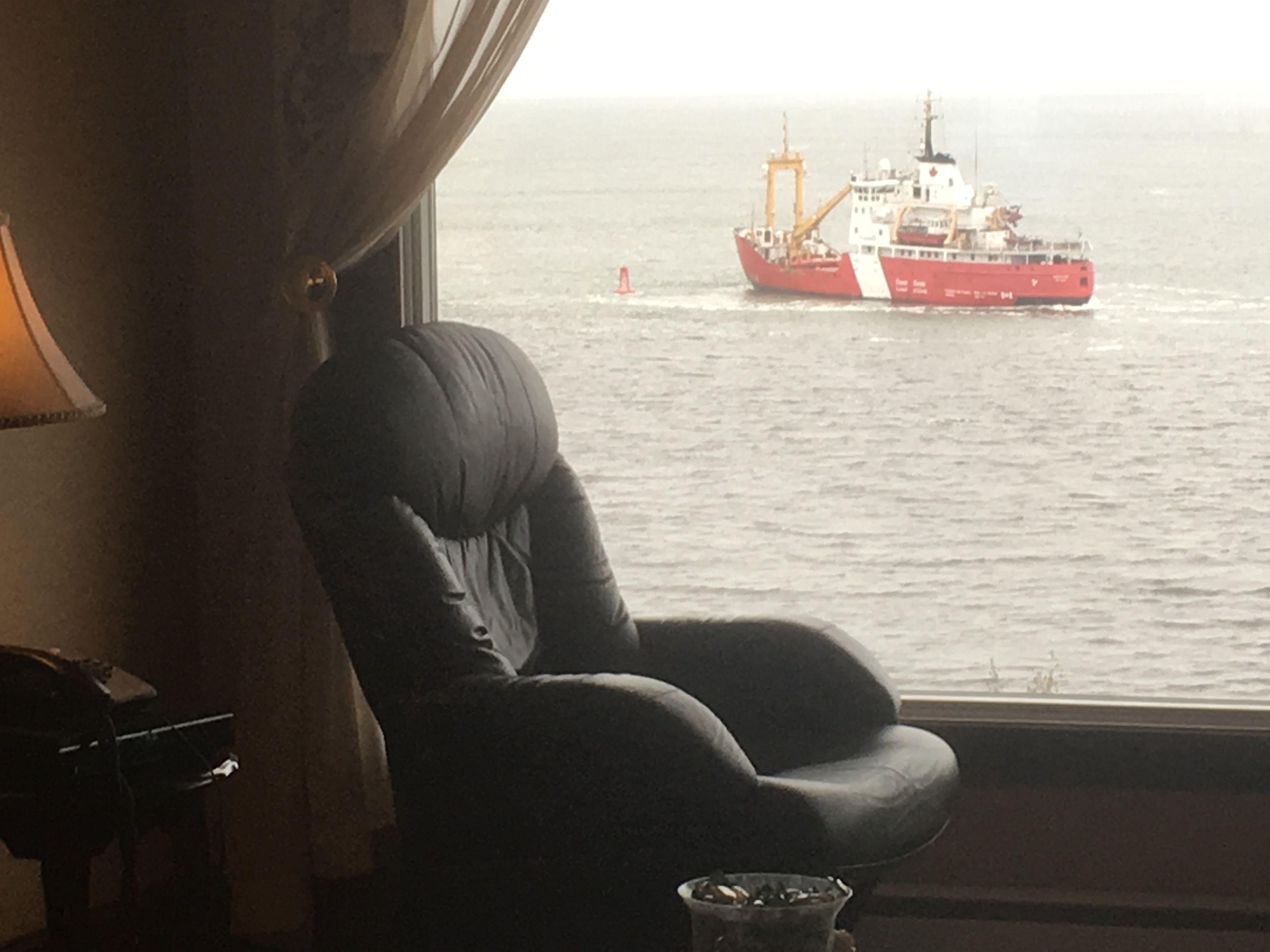 A room with a view of the sea, a chair, and a small table with a lamp.