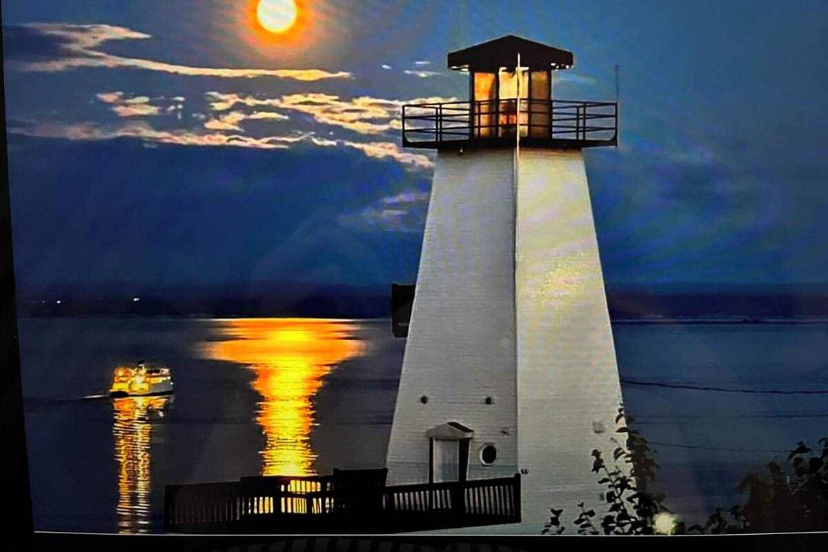Un faro con luz en la parte superior, cielo despejado y una masa de agua tranquila que refleja la luz.
