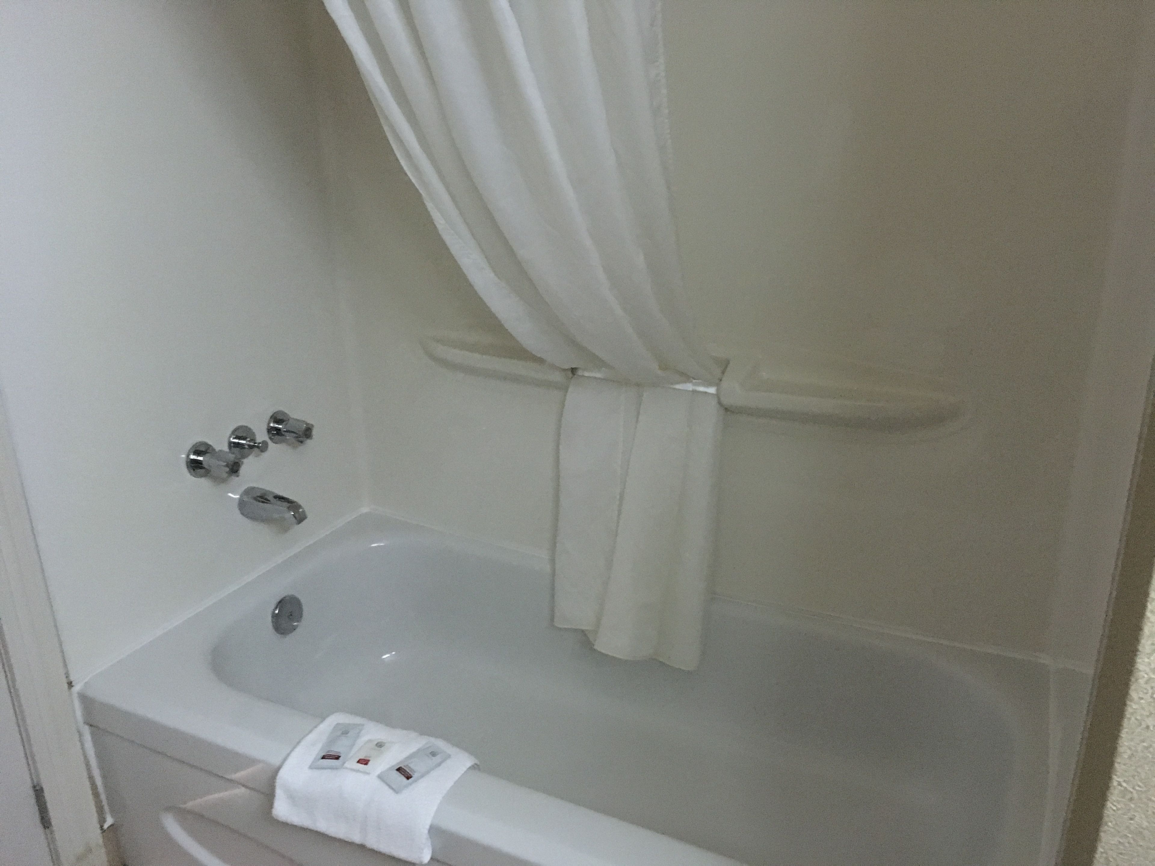 A white bathtub with a shower curtain tied at the top, a faucet, and a towel on the side.