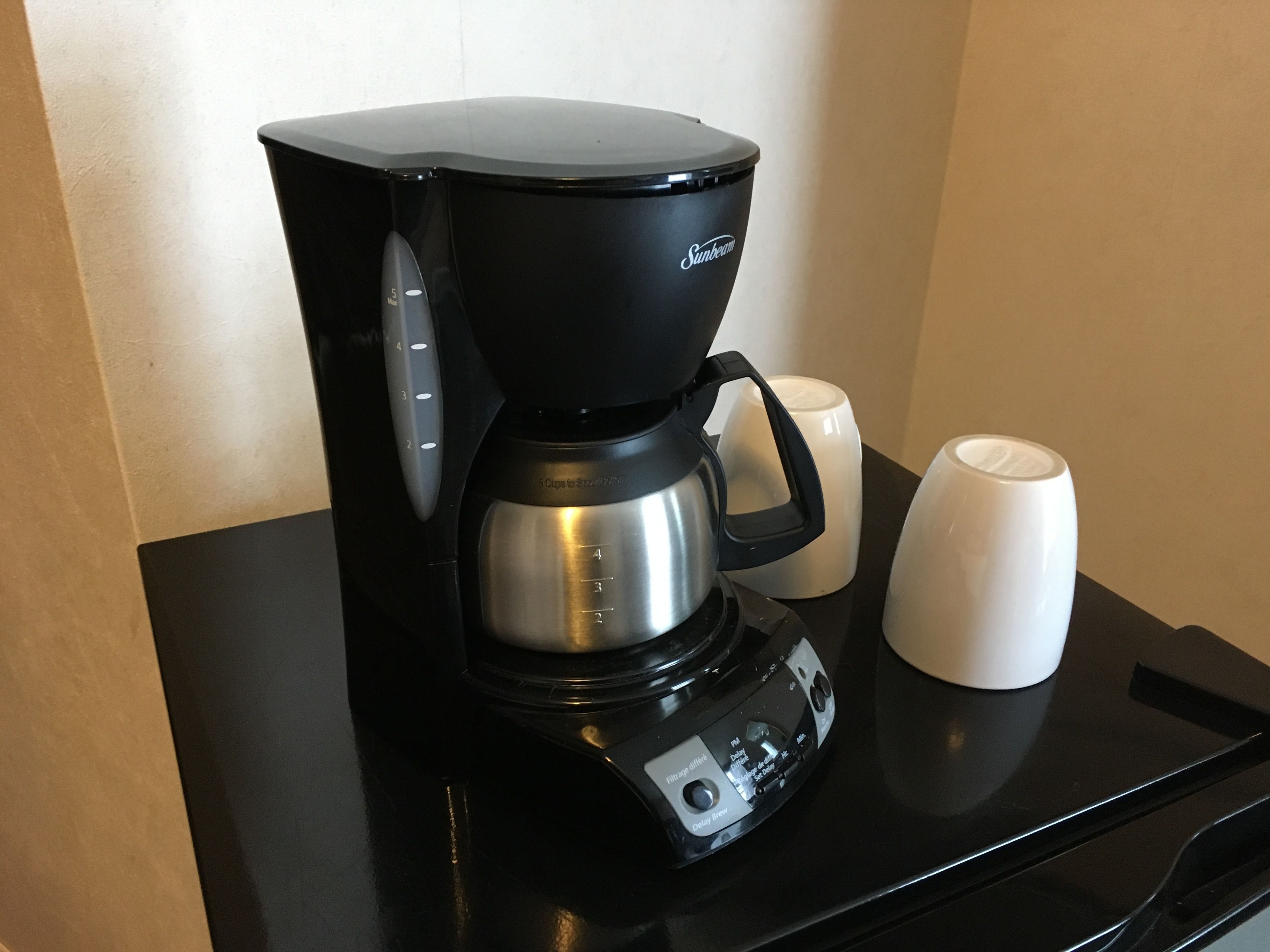 Eine schwarze Sunbeam-Kaffeemaschine mit zwei weißen Tassen auf einer schwarzen Arbeitsplatte.