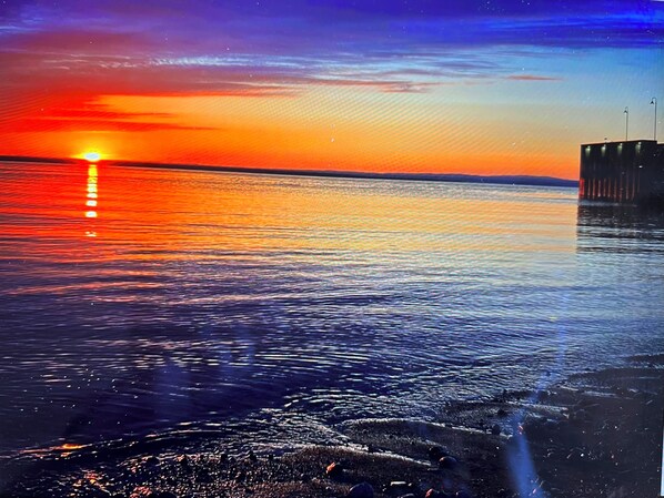 A sunset over a calm body of water with a pier extending into the water. - Motel Belvédère (Saint-Simeon)