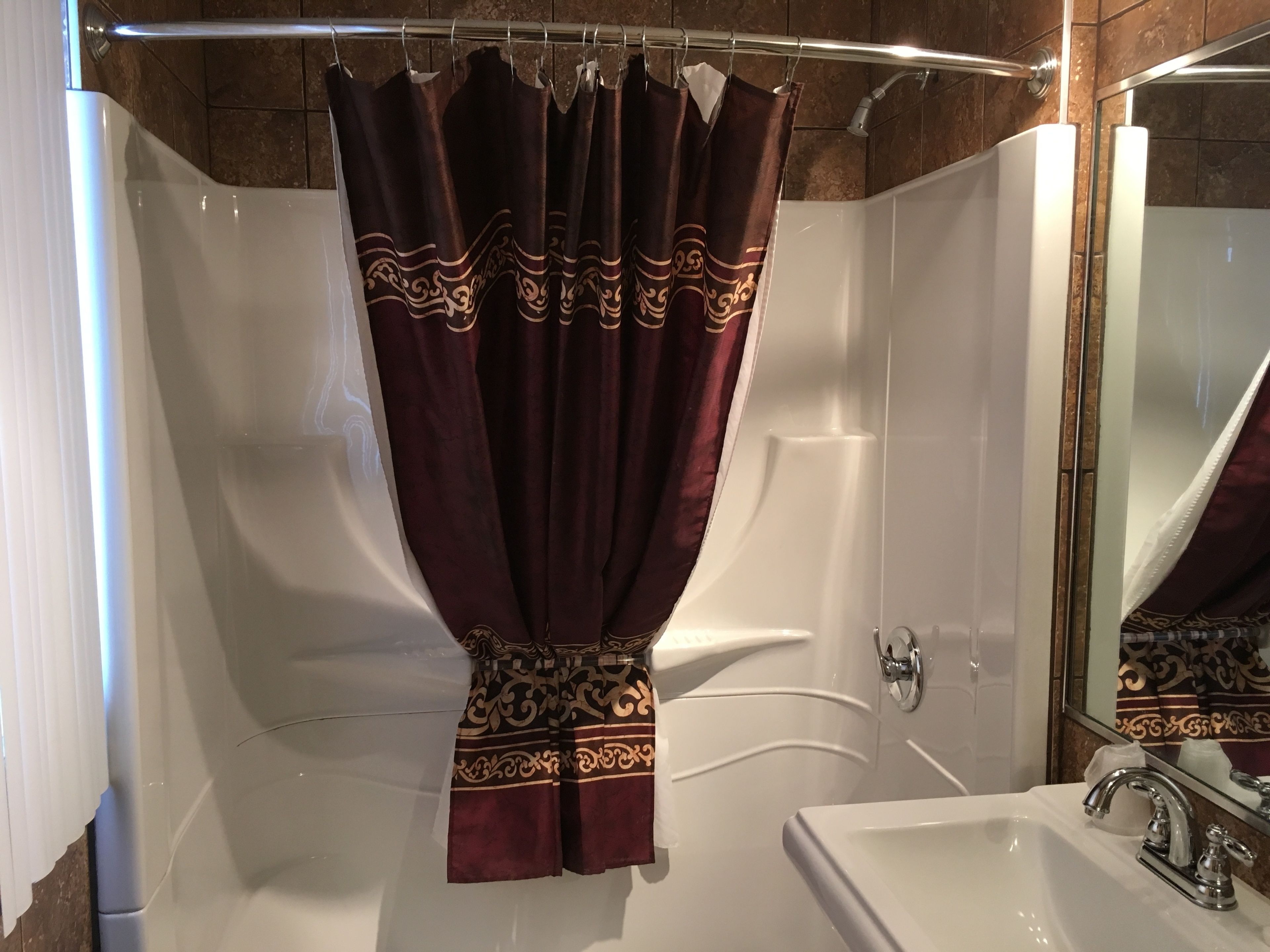 Une salle de bain avec une baignoire, un lavabo blanc et un rideau de douche orné d’un motif décoratif.