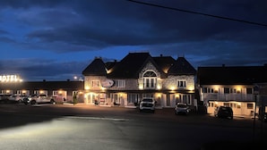 Um motel com fachada de pedra, várias janelas e um estacionamento com diversos carros.