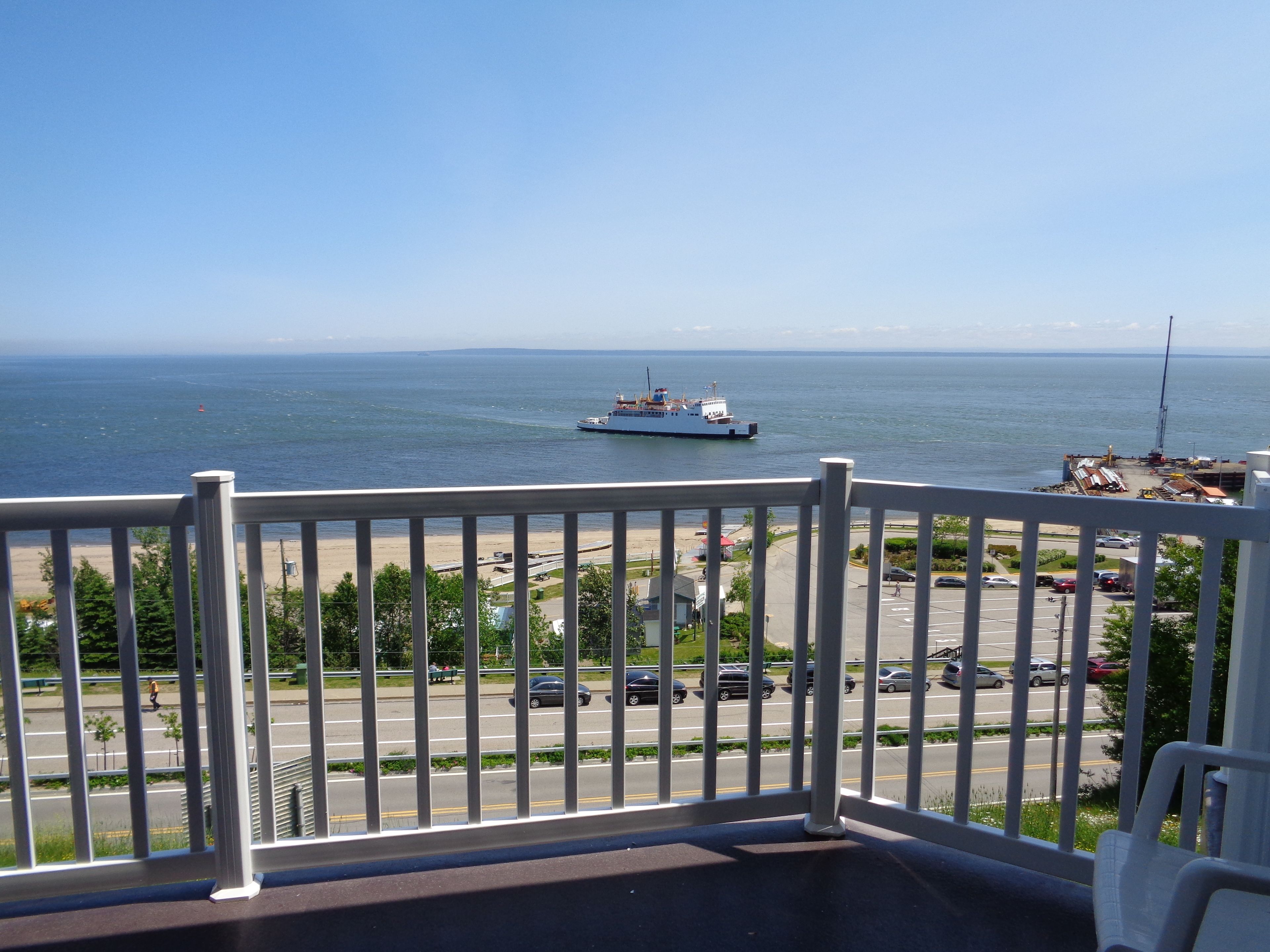 A balcony with a view of the sea, a boat, and a parking area.