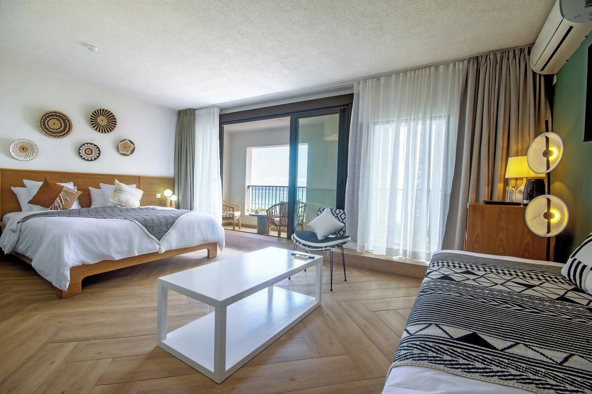 A hotel room with a bed, a sofa, a coffee table, and a balcony with a view.