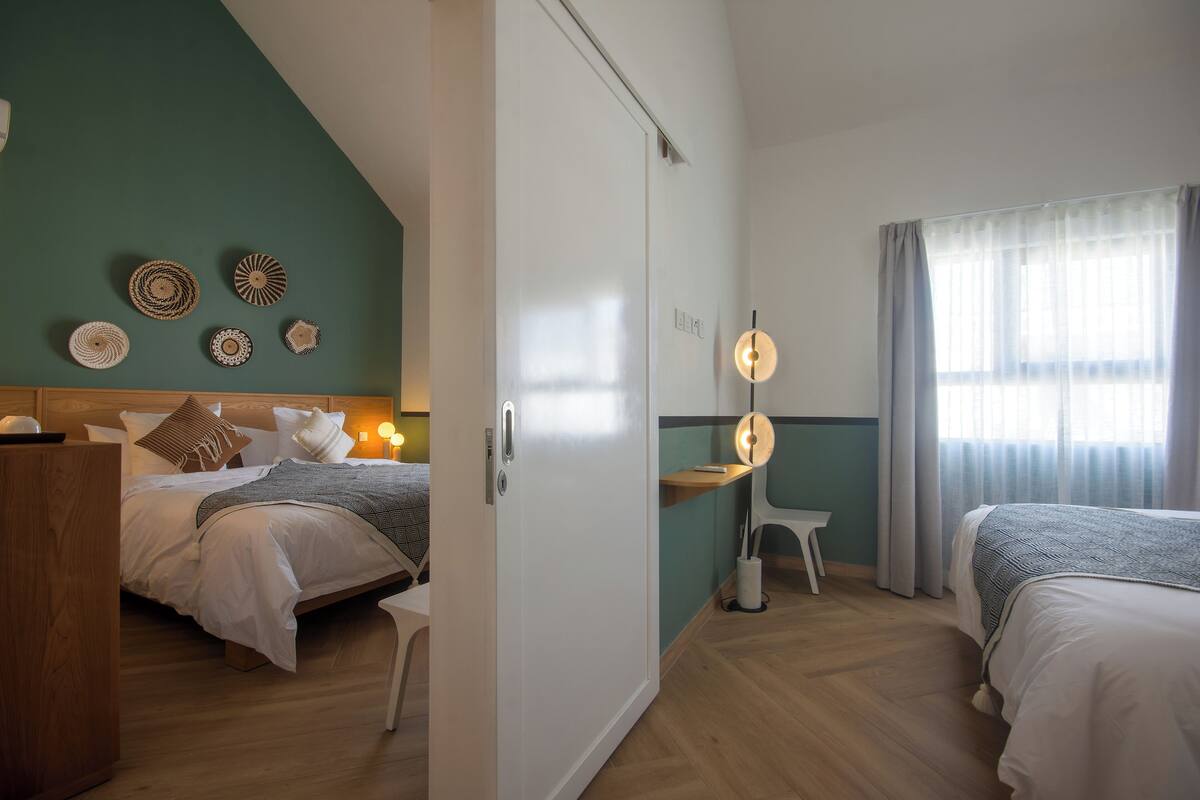 A hotel room with two beds, a desk, a wardrobe, and wall decor.