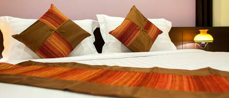 A neatly made bed with white linens and two decorative pillows, a bedside lamp, and a wooden headboard.