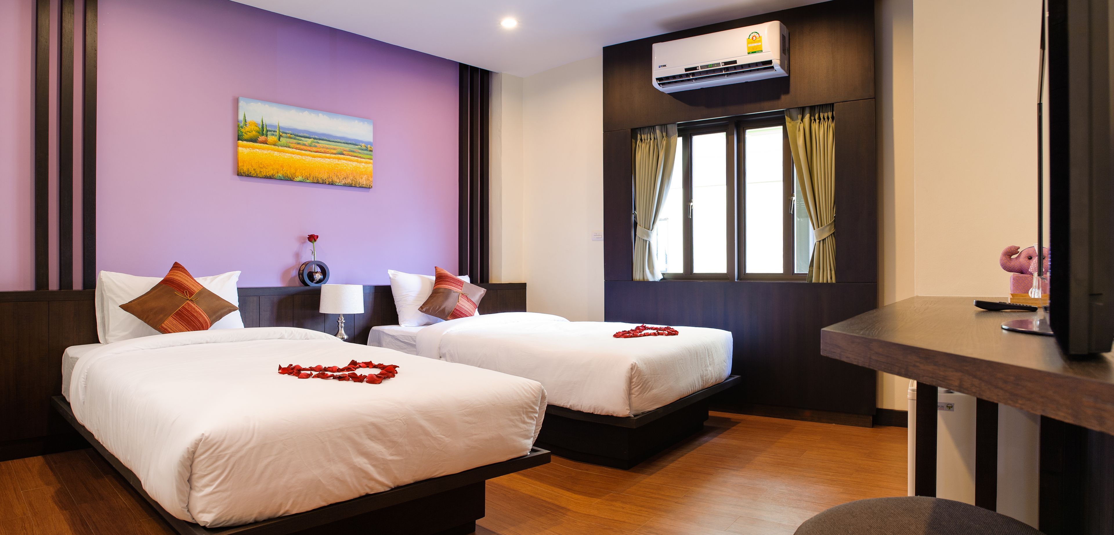 A hotel room with two beds, a desk, an air conditioner, and a window with curtains.