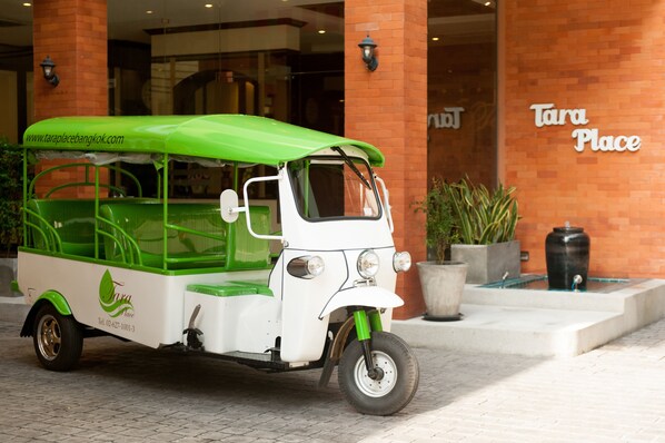 Un tuk-tuk verde y blanco estacionado frente a un edificio con un letrero que dice 'Tara Place'.