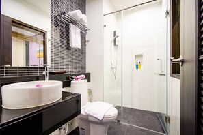 Un baño moderno con un lavamanos blanco, encimera negra y cabina de ducha de vidrio.
