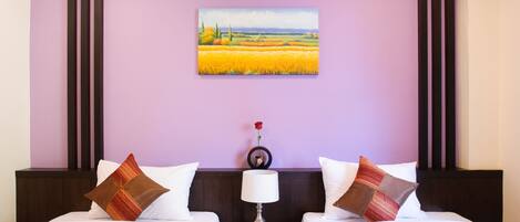 A hotel room with two beds, a nightstand with a phone, a lamp, and a painting of a field on the wall.
