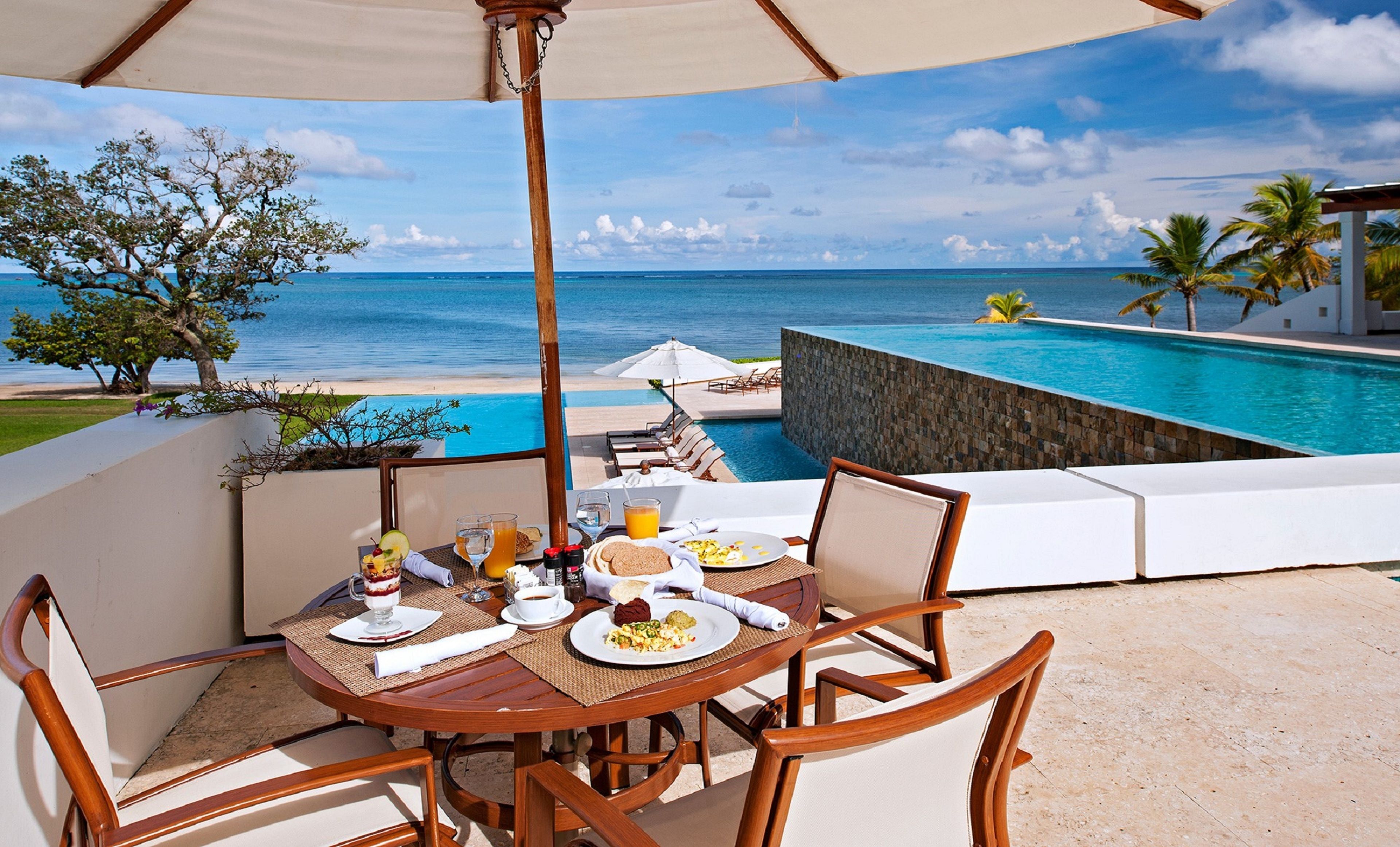 Mesa de comedor con sillas y vista a una piscina y al océano.