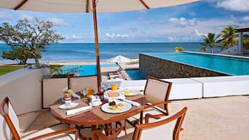 Mesa de comedor con sillas y vista a una piscina y al océano.