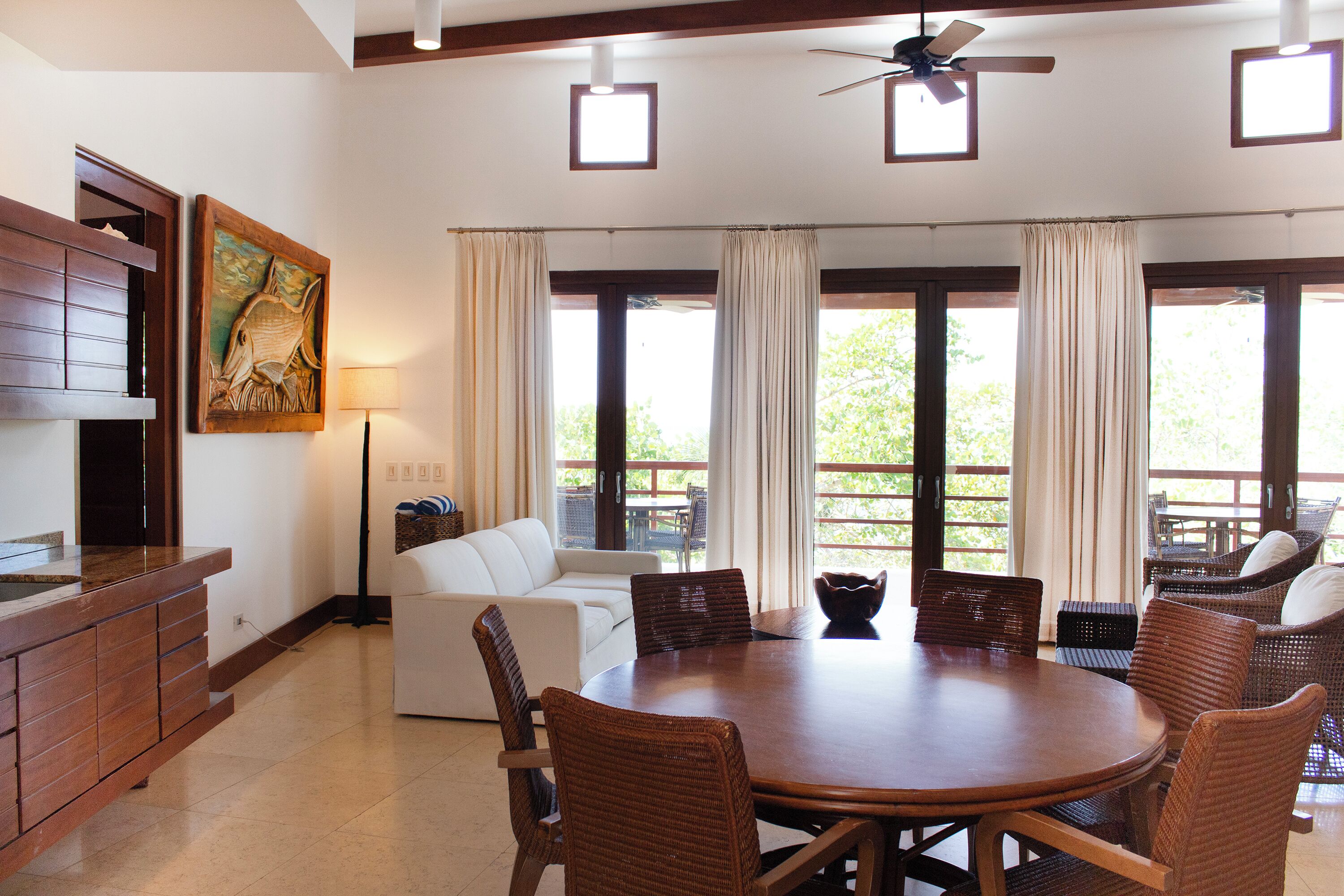 A spacious room with a dining table surrounded by wicker chairs, a white sofa, and a wooden cabinet.