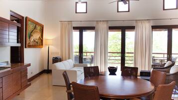 A spacious room with a dining table surrounded by wicker chairs, a white sofa, and a wooden cabinet.