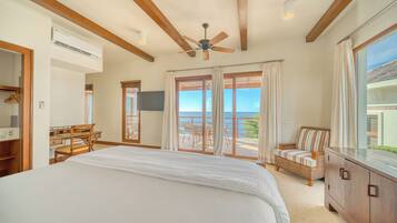A bedroom with a large bed, a ceiling fan, a TV, and a view of the sea through the sliding doors.