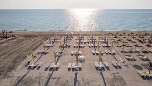 Ein Strand mit mehreren Reihen Sonnenliegen und Sonnenschirmen, ein freier Blick auf das Meer und ein weiter Horizont.