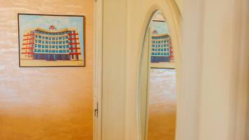 Habitación de hotel con una puerta, un cuadro enmarcado de un edificio en la pared y un espejo que refleja la misma imagen.