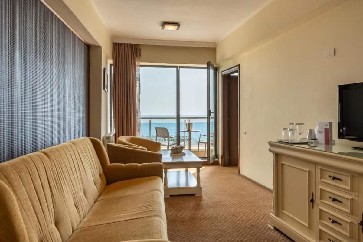 Habitación de hotel con sofá, una mesita, televisor y vistas al mar.